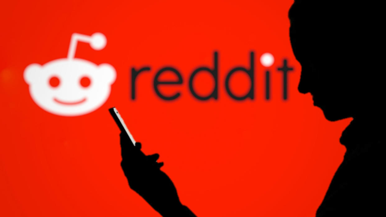  silhouette man using smartphone with Reddit logo on blurred background 