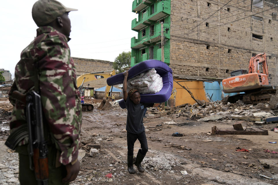 A resident carries belongings as excavators bring down houses in the Mathare area of Nairobi, Kenya Wednesday, May. 8, 2024. The Kenyan government ordered the evacuation of people from flood-prone areas, resulting in the demolition of houses and the loss of at least one life in the melee caused by the forced evictions. (AP Photo/Brian Inganga)