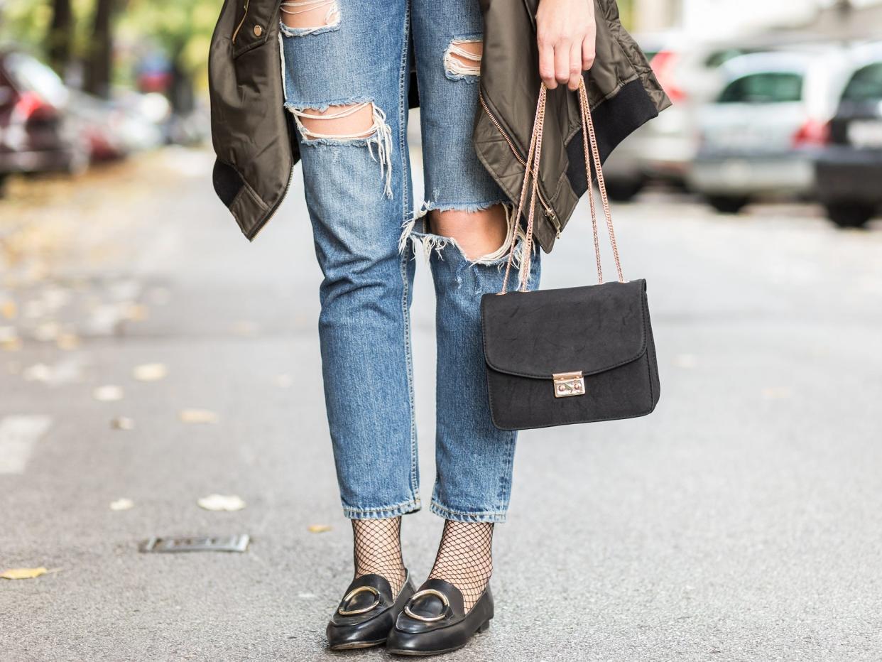 woman from legs down wearing ripped jeans, fish net tights, and loafers