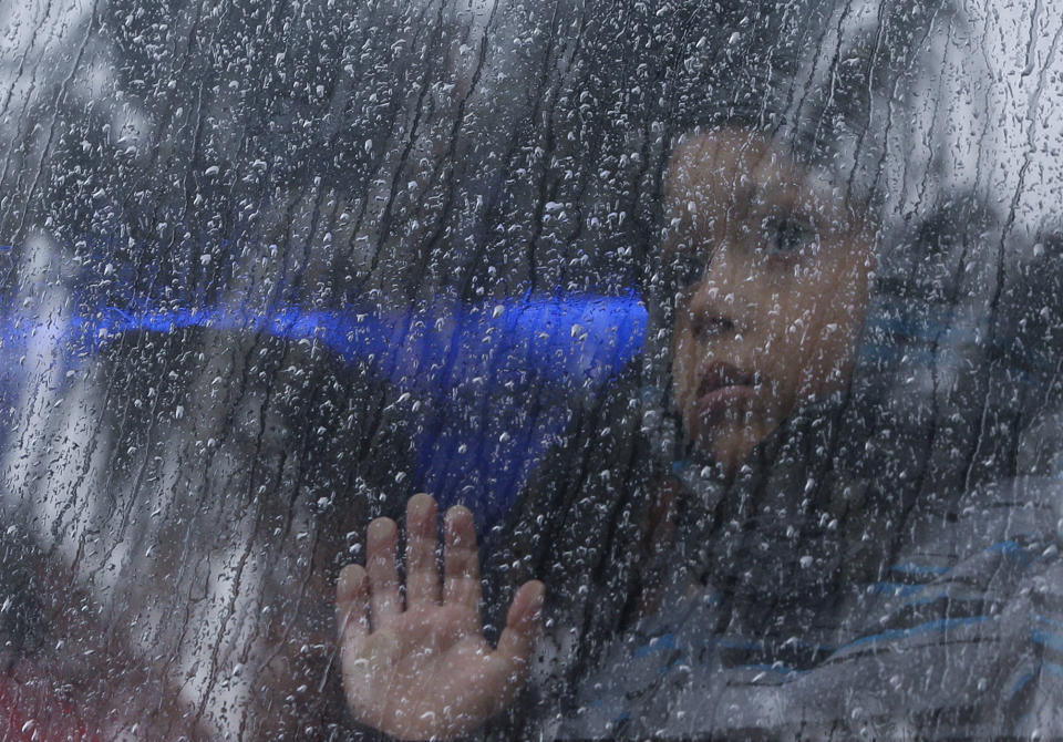 FILE - A migrant child looks out in the rain from a bus carrying Central Americans from the Barretal migrant shelter to an ongoing job fair where migrants can get help with work permits and local jobs in Tijuana, Mexico, Dec. 6, 2018. Many of the more than 2,000 migrants living at the Barretal shelter were taking the opportunity to legalize their stay in Mexico and find work while they consider whether to continue trying to reach the U.S. (AP Photo/Rebecca Blackwell, File)