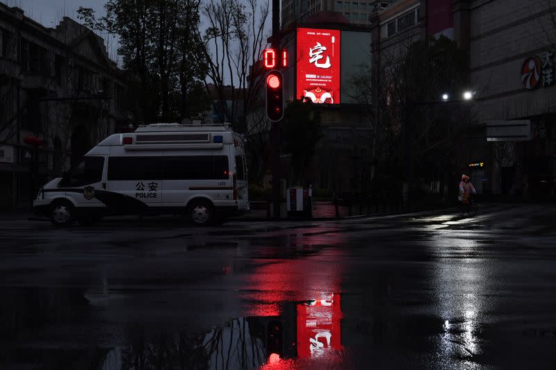 Sign advising residents to stay at home is seen on a building near a police vehicle in Wuhan