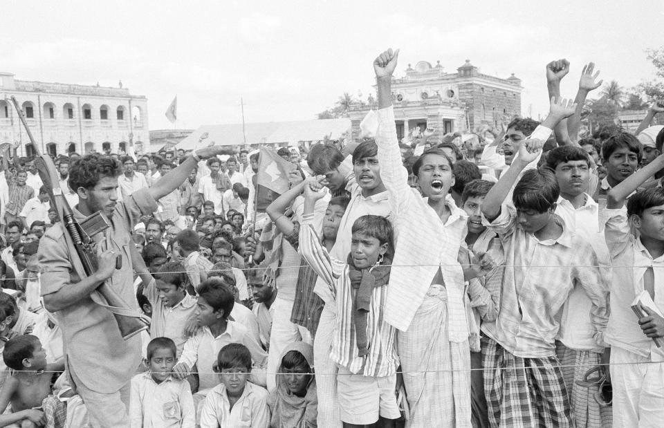 FILE - In this Dec. 11, 1971, file photo, a Mukti Bahini soldier, left, tries to keep the crowd under control as they cheer the acting Bangladesh president and the acting government during a public meeting in Jessore, East Pakistan. The city Hall with Indian soldiers standing guard on the roof is seen behind. Bangladesh is celebrating 50 years of independence this year. (AP Photo, File)