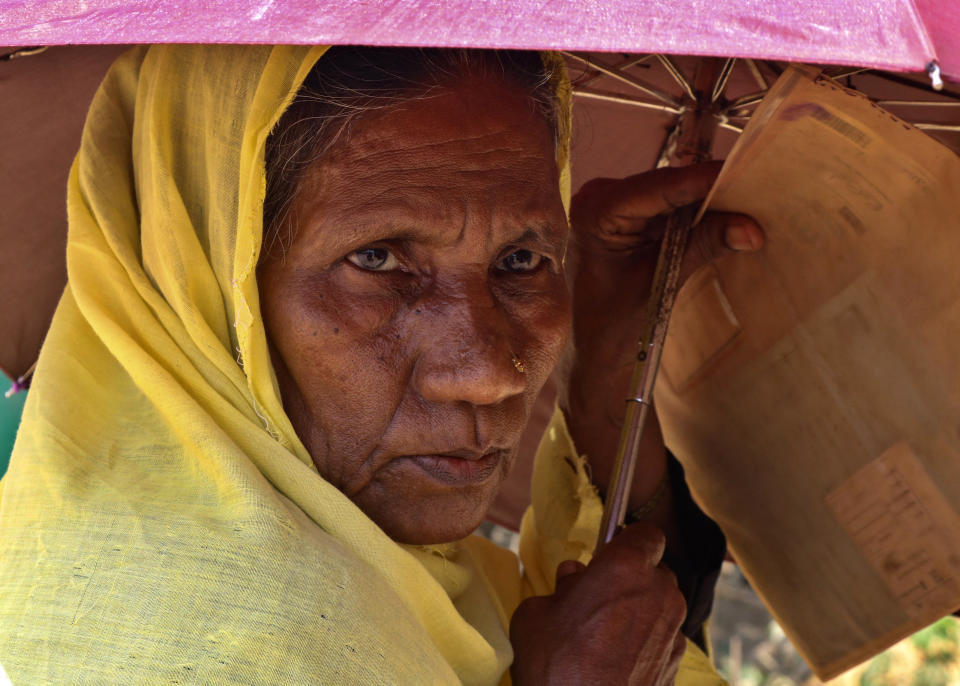 In this April 15, 2020 photograph, a Rohingya refugee woman holds an umbrella as she waits to collect food aid at the Kutupalong refugee camp in Cox's Bazar, Bangladesh. There's been little if any coronavirus testing in Cox's Bazar, where more than a million members of Myanmar's Rohingya Muslim minority are packed into the world's largest refugee camp. (AP Photo/Shafiqur Rahman)