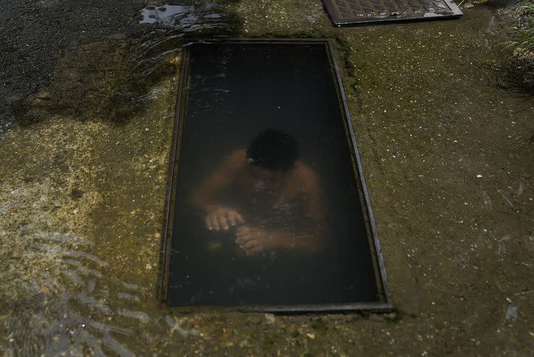 Un niño se sumerge para refrescarse en el sitio de una tubería de agua rota en una calle de Caracas, Venezuela, el 27 de julio 

