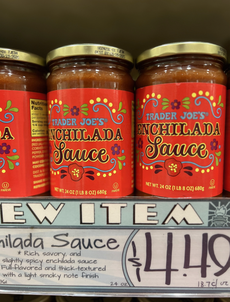 Two jars of Trader Joe's enchilada sauce on a shelf with a price tag indicating $4.49 per jar