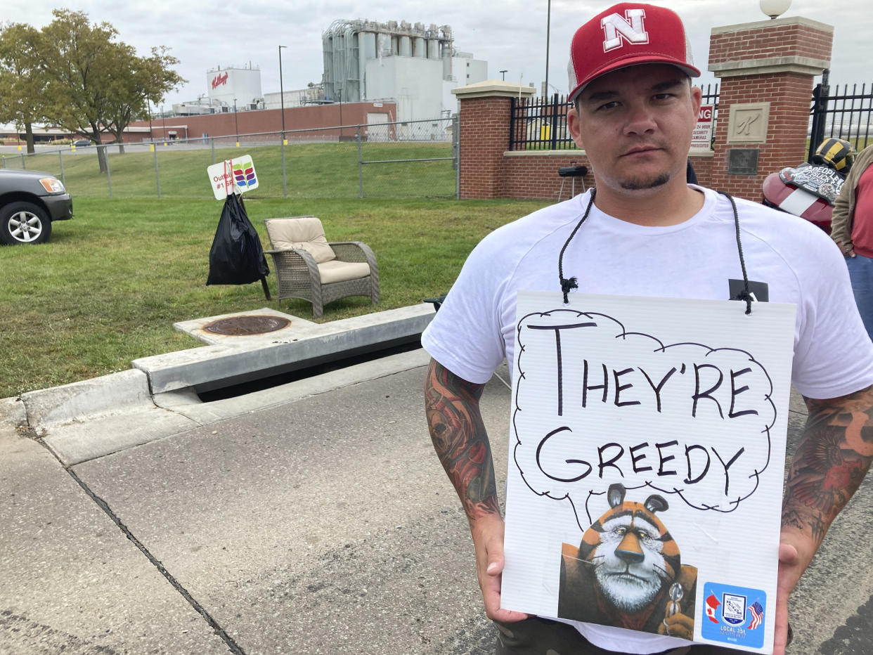 A Kellogg's employee on strike stands with a sign around his neck that says: They're Greedy.