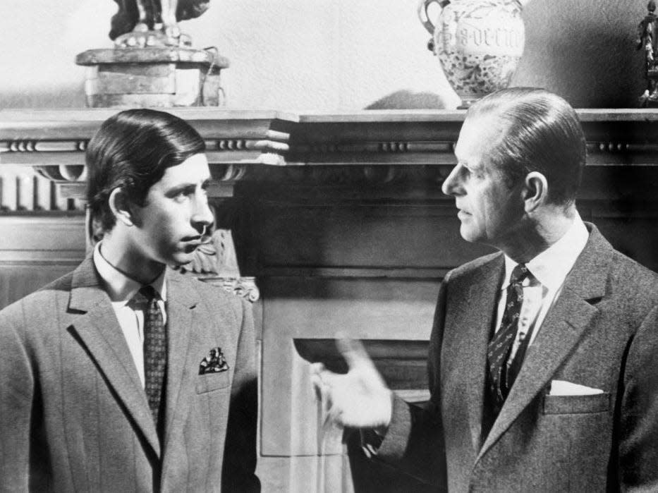 A black and white photo of Prince Charles talking to his father Prince Philip in front of a fireplace at Sandringham.