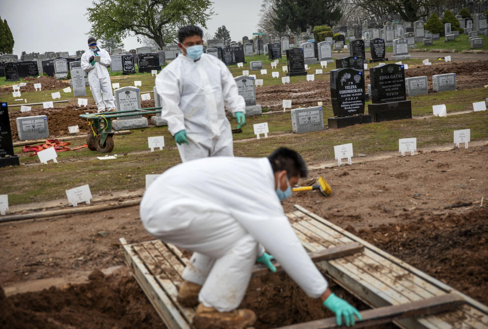 Rabbi Shmuel Plafker, rear, finishes a prayer during the burial service for David Tokar as gravediggers prepare a plot for the next burial at Mount Richmond Cemetery in the Staten Island borough of New York, Wednesday April 8, 2020. When Plafker arrives at the cemetery, it's buzzing: Vans pulling in with bodies aboard, mounds of dirt piling up as graves are dug open, a line of white signs pressed into the ground marking plots that are newly occupied. Some of the few signs of life in this anguished city are coming from those tending to the dead. (AP Photo/David Goldman)