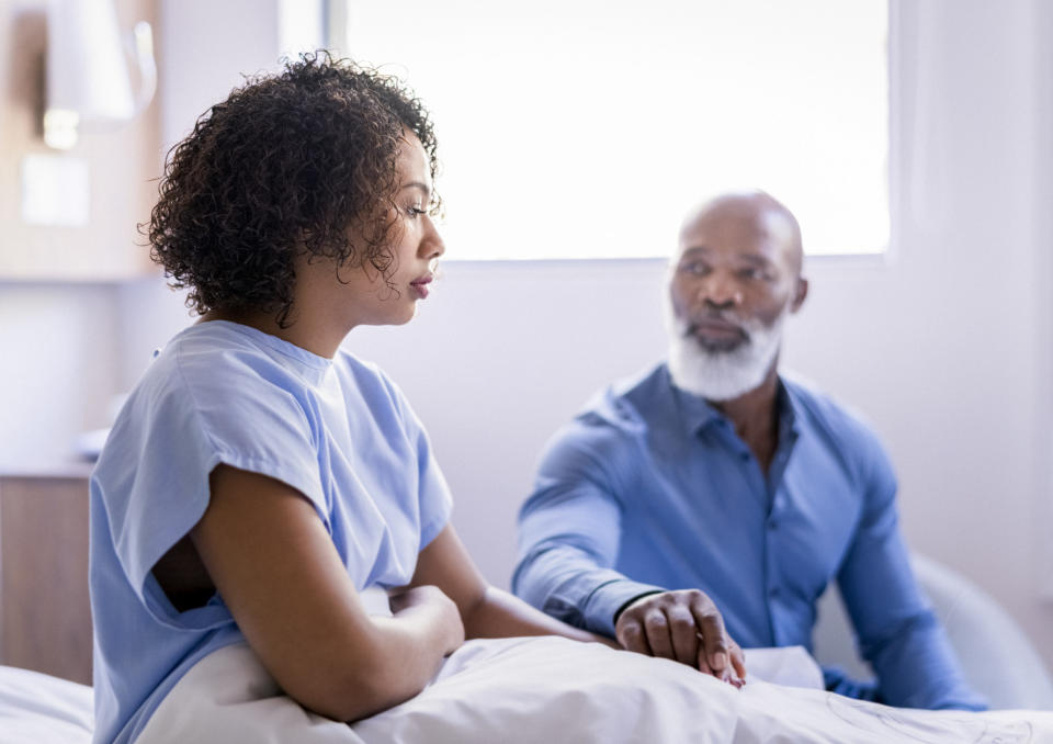 Father consoling daughter in patient gown at hospital by holding hand