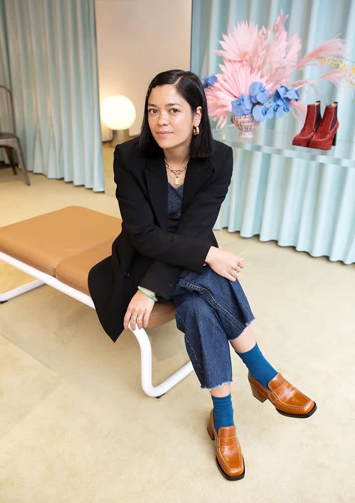 designer lauren bucquet of labucq sits in her showroom wearing a blazer, jeans, blue socks, and caramel colored square toe loafers