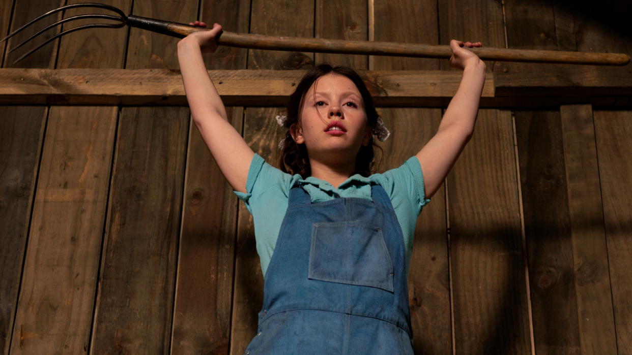  Mia Goth theatrically holds a pitchfork over her head in the barn in Pearl. 