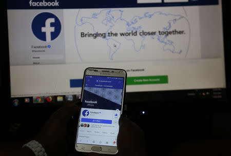 An illustration photo shows the Facebook page displayed on a mobile phone internet browser held in front of a computer screen at a cyber-cafe in downtown Nairobi, Kenya April 18, 2019. REUTERS/Stringer