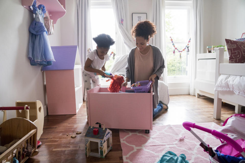 Adult and child tidying up toys in a bedroom, engaging together with a focus on organizing