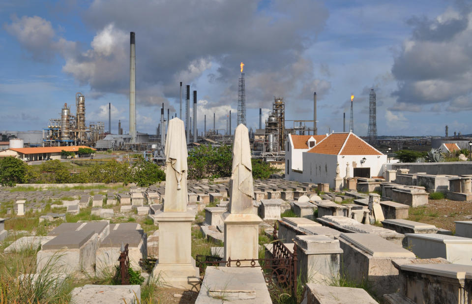 In this Nov. 12, 2012 photo, a portion of the Beth Haim cemetery, backdropped by the Isla oil refinery, is seen in Blenheim, on the outskirts of Willemstad, Curacao. Beth Haim, believed to be one of the oldest Jewish cemeteries in the Western Hemisphere, established in the 1950s and considered an important landmark on an island where the historic downtown has been designated a UNESCO World Heritage Site, is slowly fading in the Caribbean sun. Headstones are pockmarked with their inscriptions faded, stone slabs that have covered tombs in some cases for hundreds of years are crumbling into the soil, marble that was once white is now grey, likely from the acrid smoke that spews from the oil refinery that looms nearby. (AP Photo/Karen Attiah)