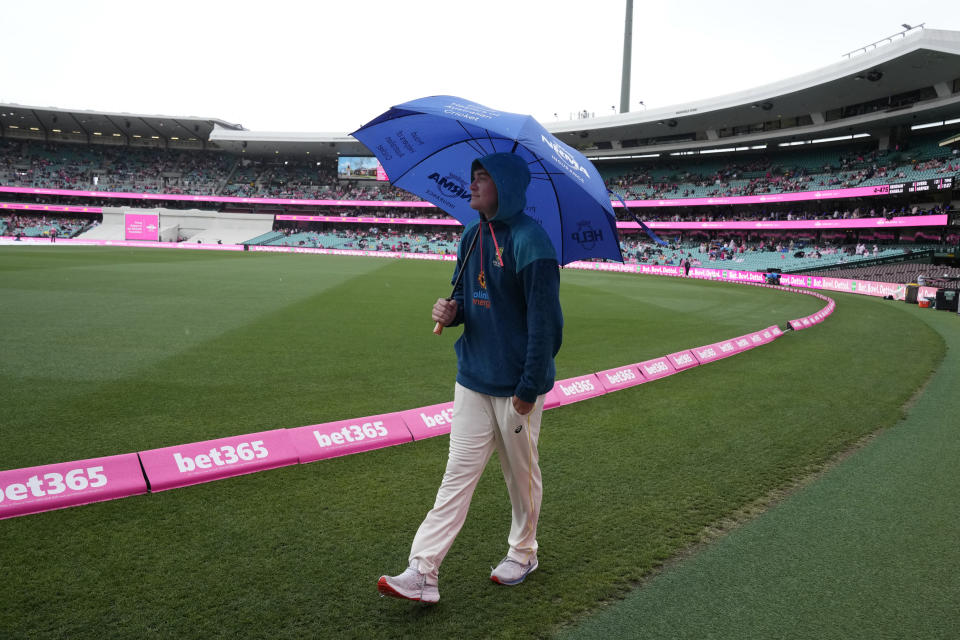 Australia's Matt Renshaw carries an umbrella as he walks along the boundary during a rain delay during the third day of the cricket test match between Australia and South Africa at the Sydney Cricket Ground in Sydney, Friday, Jan. 6, 2023. (AP Photo/Rick Rycroft)