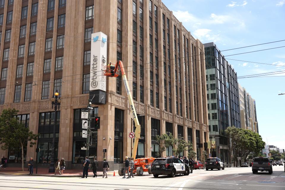A large crane that has been parked on the road outside an office building to allow a worker to remove letters from a "Twitter" sign.