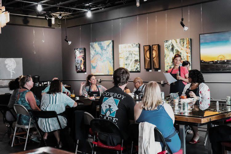 group of people sitting around a table at an art studio taking a fun art class