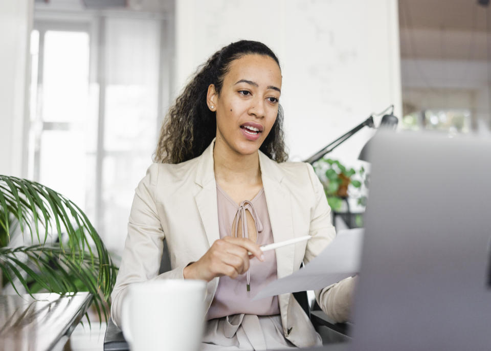 Businesswoman holding a document having video call on laptop while sitting on her office desk. Female entrepreneur having video conference on her laptop.