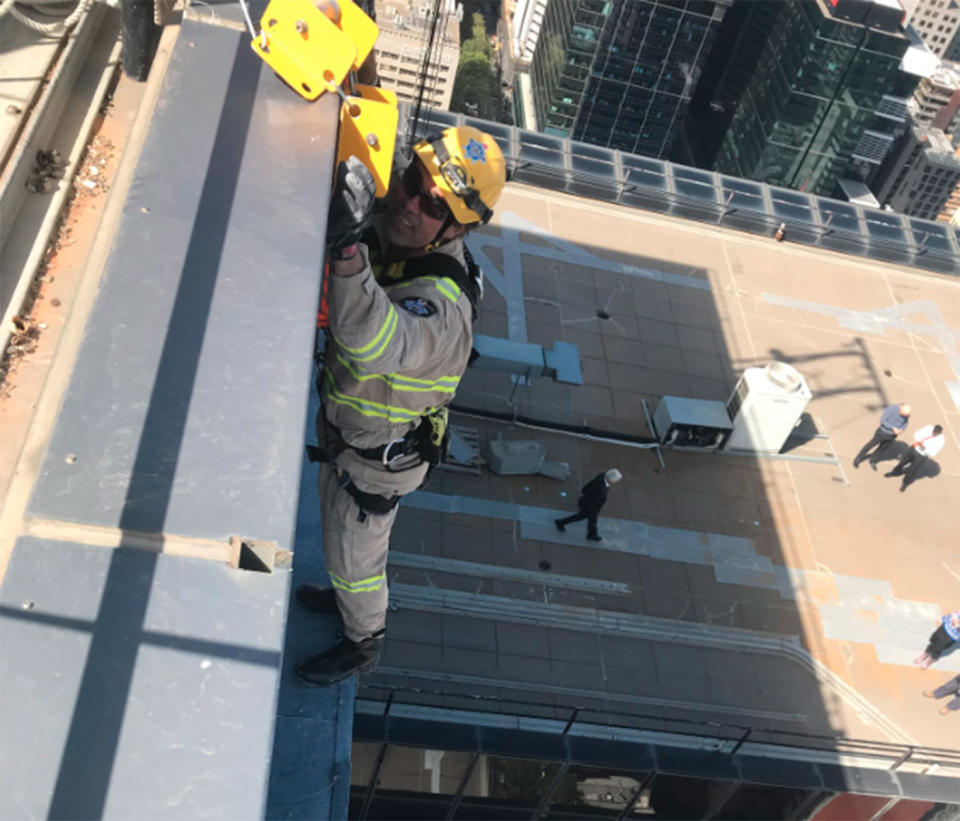 Firefighters abseiled down a high-rise building in Melbourne’s CBD to remove a dangling sign dislodged by wild weather. Source: 7 News