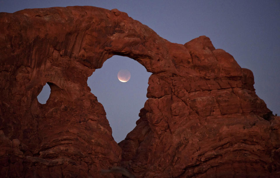 FILE - In this Dec. 10, 2011, file photo, a lunar eclipse is framed within Turret Arch at Arches National Park near Moab, Utah. The family of a women's rights activist from Uganda sued the National Park Service this month after she was decapitated last year by a gate at Utah's Arches National Park. The gate had been left unlatched against federal policy for two weeks before it struck Esther Nakajjigo in June 2020, according to the lawsuit filed in Denver. (AP Photo/Julie Jacobson, File)