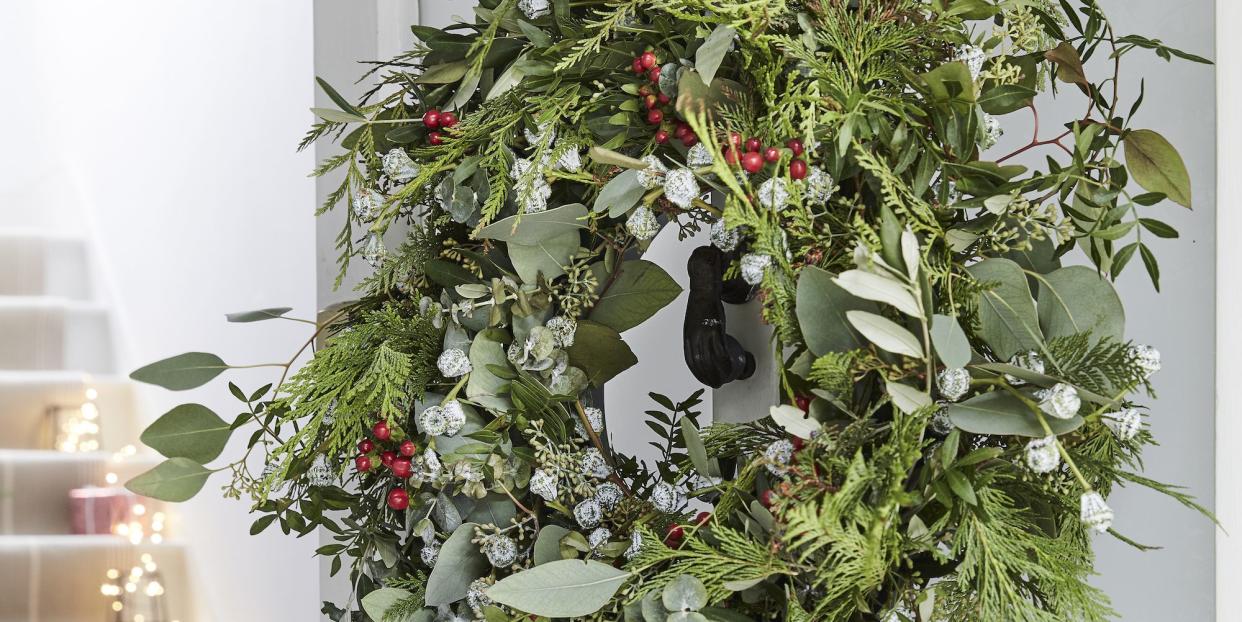 real handmade green wreath on the front of an open white door, staircase in the background