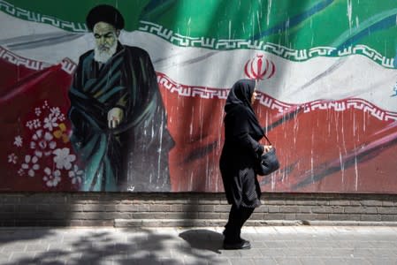 An Iranian woman walks in front of a mural of Iran's late leader Ayatollah Ruhollah Khomeini in Tehran