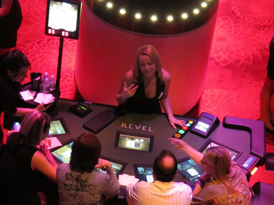 In this March 28, 2012, photo, Ludmilla Kaliafa, an E-Dealer at Revel in Atlantic City N.J., chats with gamblers on the first night the $2.4 billion casino resort allowed people to gamble. It was the first of three invitation-only test nights before Revel opens to the public on Monday, April 2. (AP Photo/Wayne Parry)