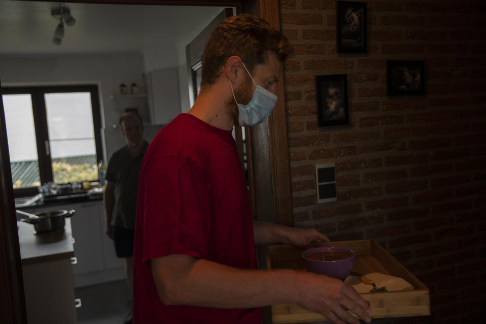 In this photo taken on Wednesday, April 29, 2020, Frederico Taramaschi, the son of Diane Wanten, 61, brings a meal to his mother as his father Francesco Taramaschi, left, walks in the background in Alken, Belgium. Diane Wanten, 61, was recently released into home quarantine after being treated for two weeks in the hospital intensive care ward of the Jessa Hospital for COVID-19 coronavirus patients. (AP Photo/Francisco Seco)