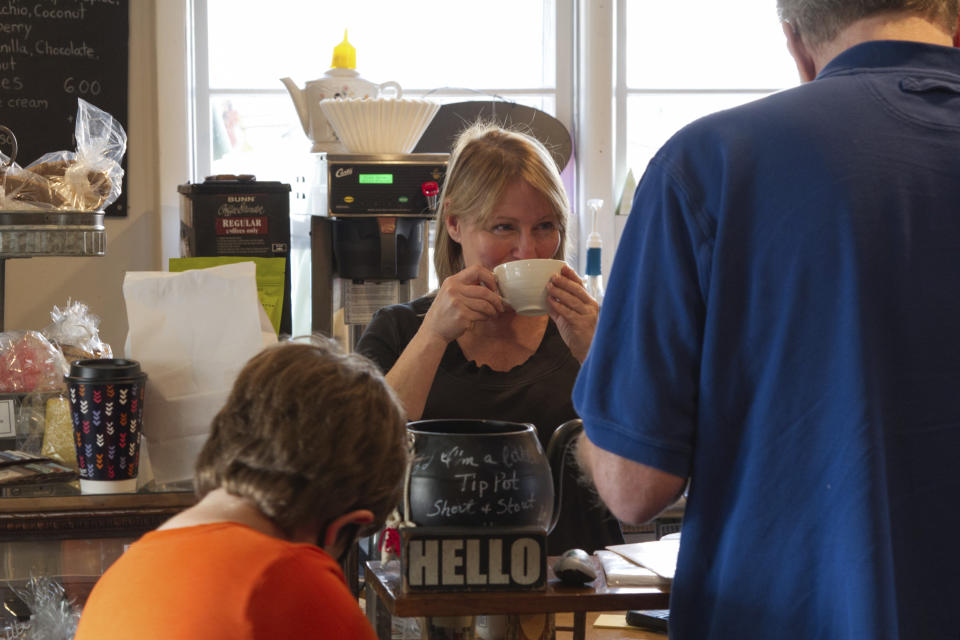 Maureen Donnelly Morris sips from her own brew while greeting neighbors at Back Street Brews in Lovettsville, Va., Dec. 16, 2021. When she came from nearby Leesburg several years ago to open her café in what was then a craft store, strangers showed up to help, bringing plants, solar lights, concrete for her parking sign footings and more. A sense of community has so far survived the political divisions ripping at America and the town. (AP Photo/Cal Woodward)