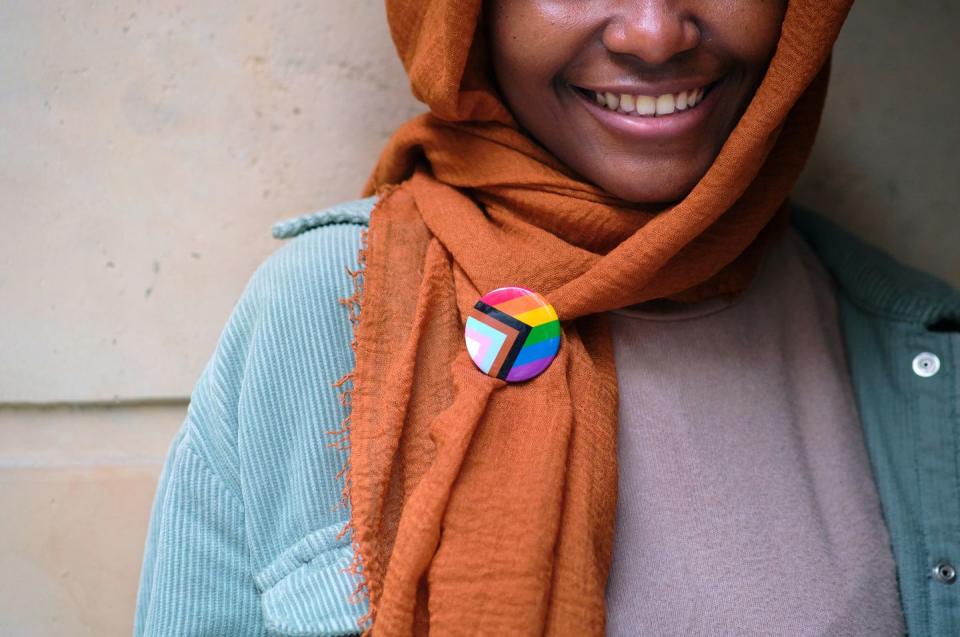 a smiling muslim woman wearing a lgbtq pin on her clothing