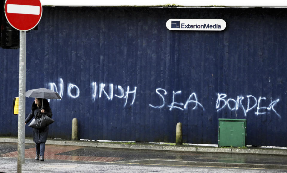 A woman walks past past graffiti with the words 'No Irish Sea Border' in Belfast city centre, Northern Ireland, Wednesday, Feb. 3, 2021. Politicians from Britain, Northern Ireland and the European Union are meeting to defuse post-Brexit trade tensions that have shaken Northern Ireland’s delicate political balance. British Cabinet minister Michael Gove, European Commission Vice President Maros Sefcovic and the leaders of Northern Ireland’s Catholic-Protestant power-sharing government will hold a video conference to discuss problems that have erupted barely a month after the U.K. made an economic split from the 27-nation EU. (AP Photo/Peter Morrison)