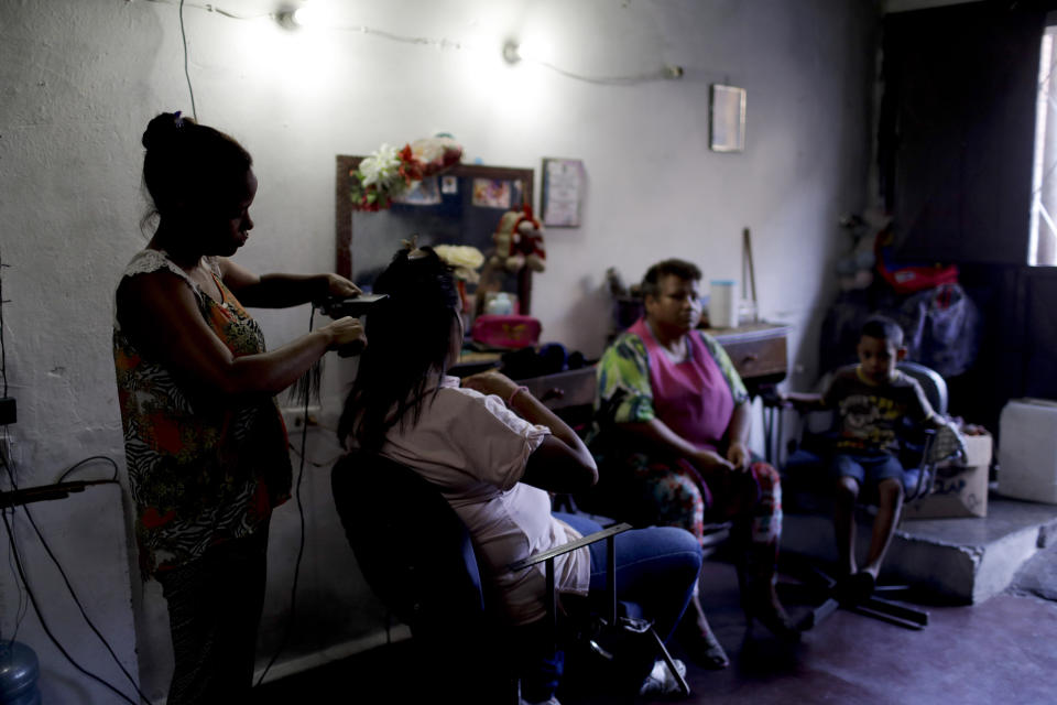 Hair dresser Rosevel Velazquez attends a customer at her beauty salon, which she runs out of her home in Caracas, Venezuela, Wednesday, March 20, 2019. Some beauty salon workers are bartering deals with their clients, getting food in exchange for hair stylings, manicures and pedicures. (AP Photo/Natacha Pisarenko)