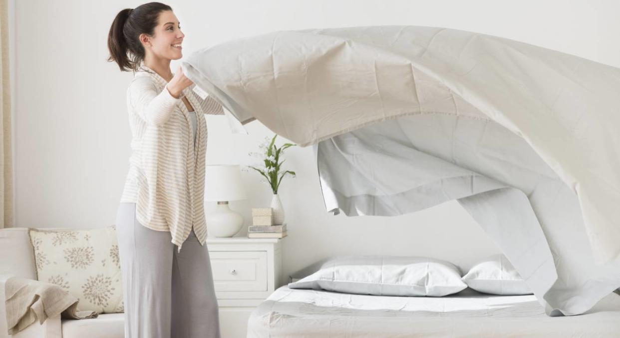 Woman making the bed with fresh sheets [Photo: Getty]