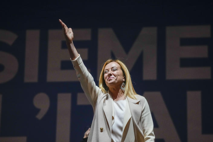 Giorgia Meloni sonrió con el brazo derecho levantado y los dedos extendidos.