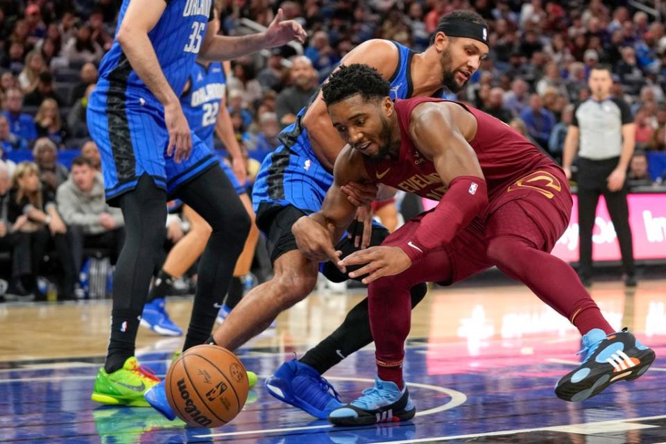 Cleveland Cavaliers guard Donovan Mitchell, right, tries a loose ball before in goes out of bounds in front of Orlando Magic guard Jalen Suggs during the first half of an NBA basketball game, Monday, Dec. 11, 2023, in Orlando, Fla. (AP Photo/John Raoux)
