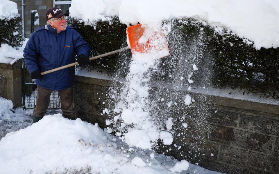 A man clears snow from his home in Ardgay, Scotland during low temperatures across the north of the country