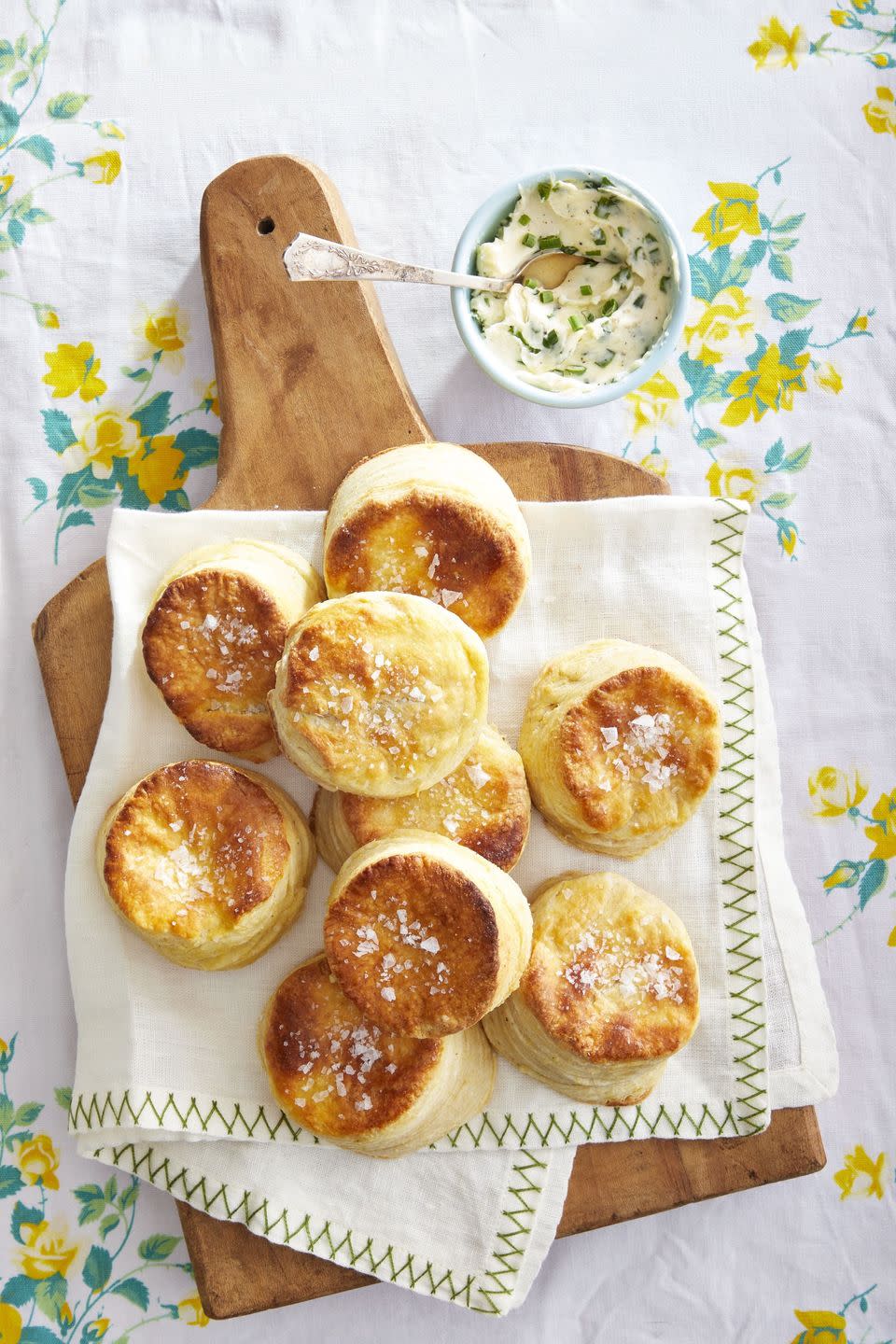 cornmeal butter biscuits piled on a wooden serving board with a small bowl of chive butter on the side