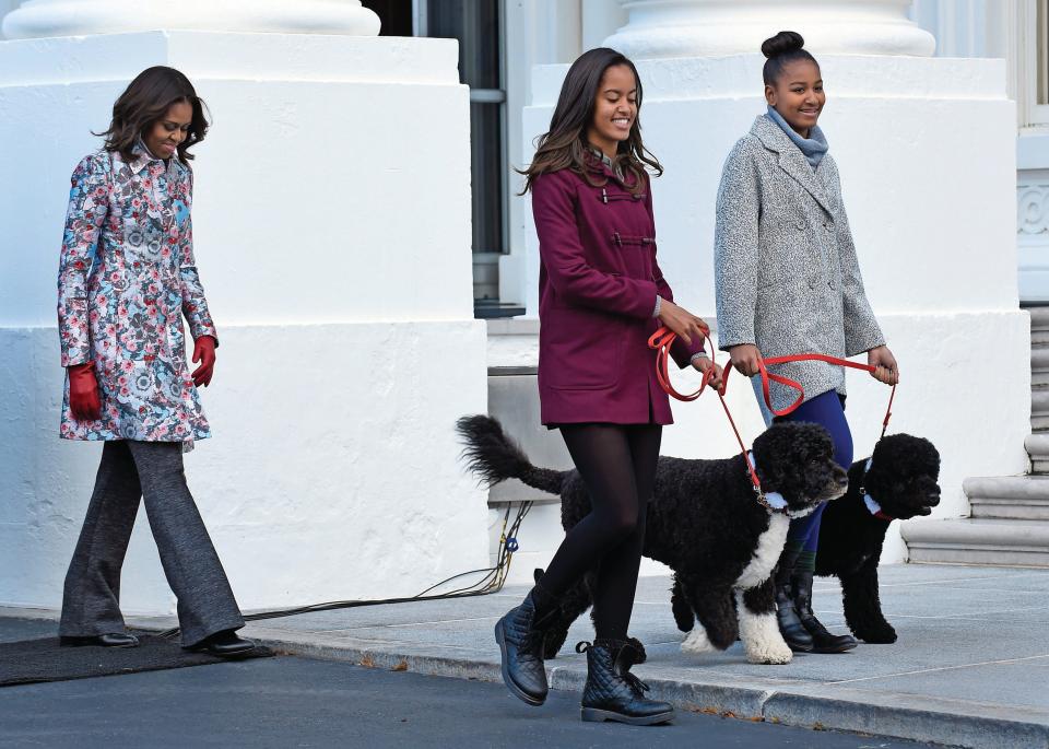 Former first lady Michelle Obama, left, follows her daughters Malia Obama, holding the leash for Bo, center, and Sasha Obama, holding the leash for Sunny, as they arrive to welcome the Official White House Christmas Tree to the White House in Washington, on Nov. 28, 2014.