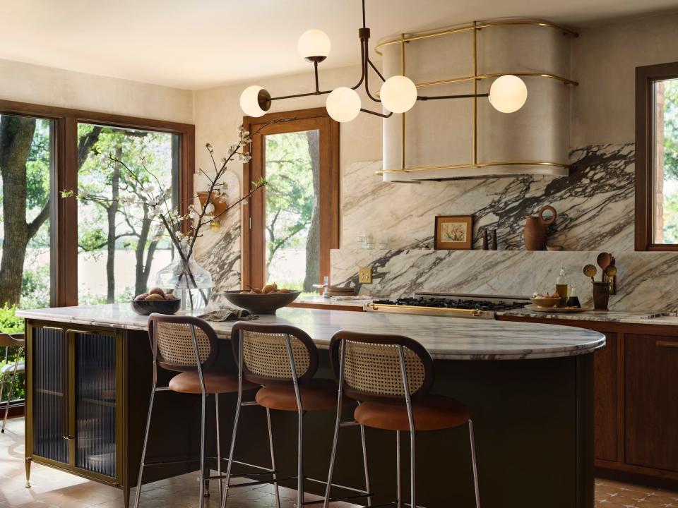 A kitchen with a large island, marble countertops and backsplash, and a large chandelier.