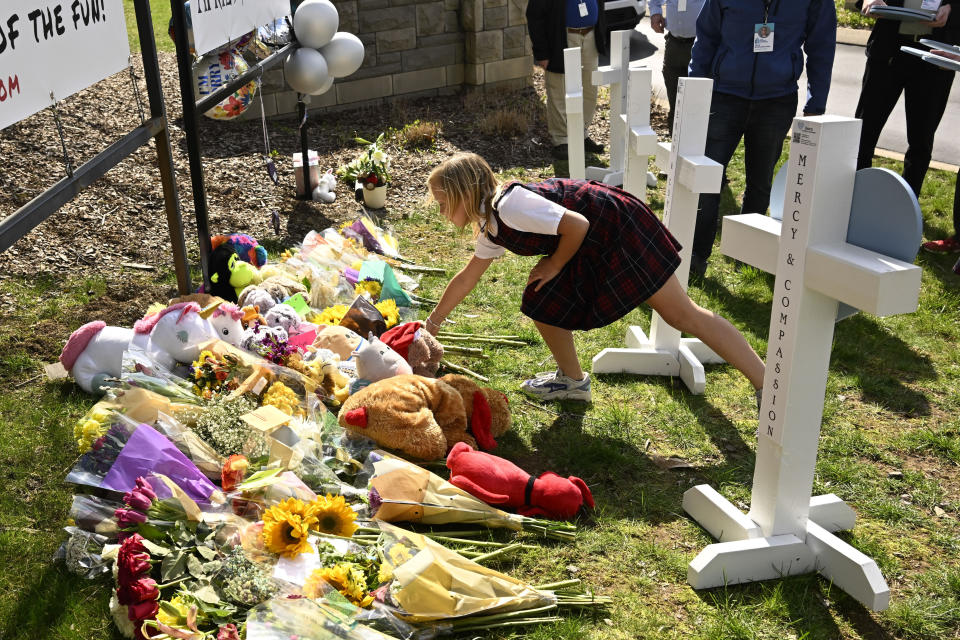 A young girl places an item at a growing memorial,Tuesday, March 28, 2023, in Nashville, at an entry to Covenant School for the victims of Monday' shooting. (AP Photo/John Amis)