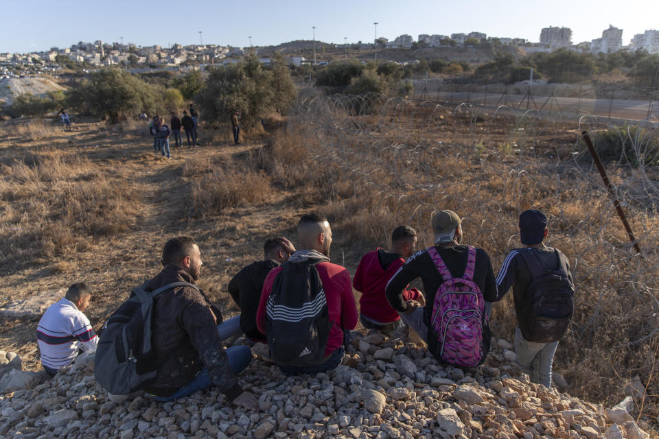 Palestinians gather by a section of Israel's separation barrier, while they wait for the Israeli army to allow them to cross the fence, in the West Bank village of Nilin, west of Ramallah, Sunday, Nov. 7, 2021. (AP Photo/Nasser Nasser)