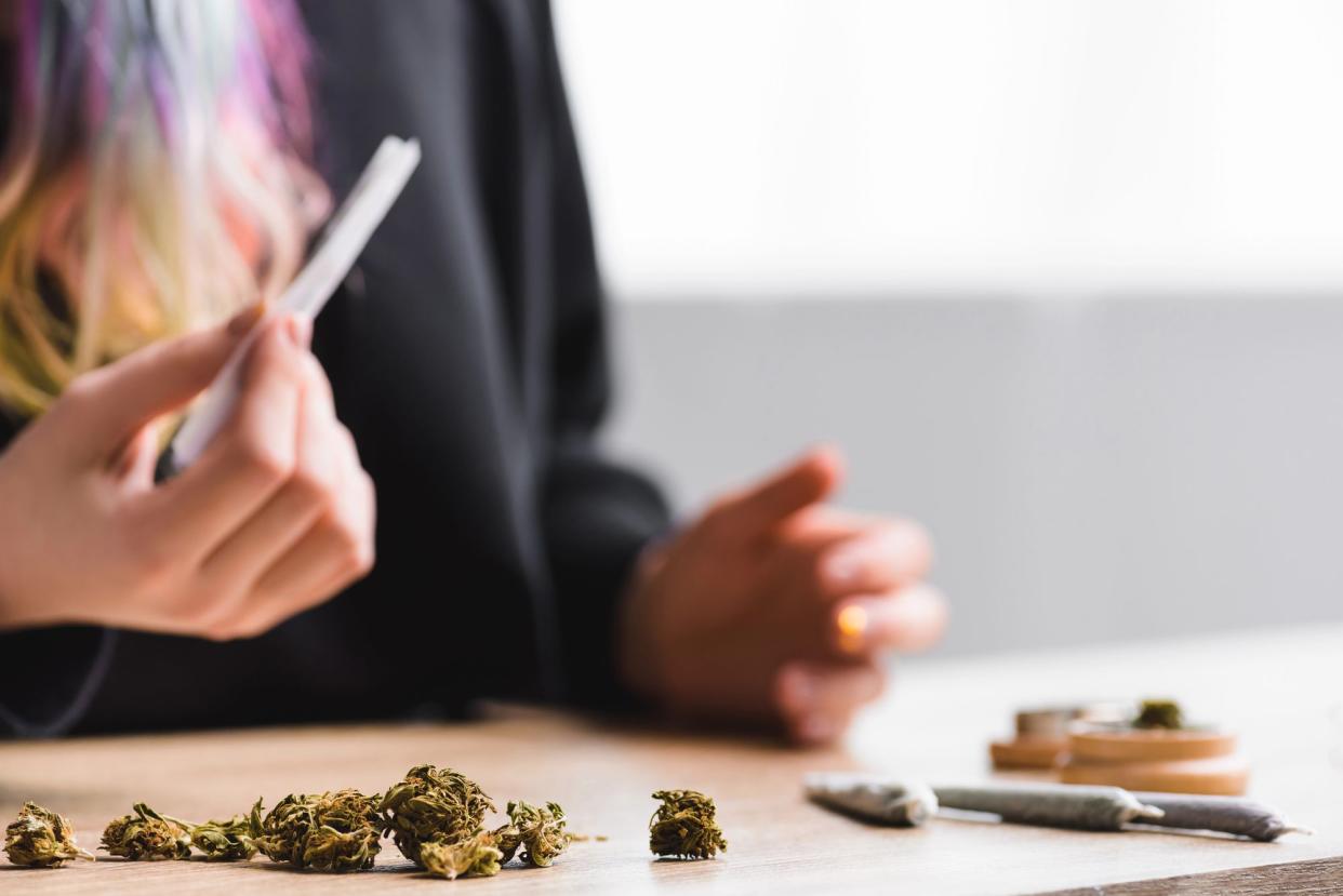 Mid-Section of Woman Holding a Joint, Marijuana on the Table, Blurred With Colorful Hair