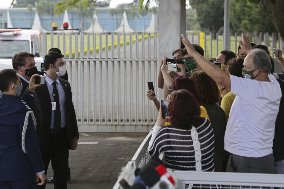 Brazil's President Jair Bolsonaro, second from left, listens to supporters saying a prayer for him as he leaves his official residence of Alvorada palace in Brasilia, Brazil, Monday, May 25, 2020. They wear face masks amid the new coronavirus pandemic. (AP Photo/Eraldo Peres)