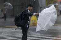 A man struggles with his umbrella against strong wind at a crossing in Shibuya district, Tokyo Saturday, Oct. 12, 2019. Tokyo and surrounding areas braced for a powerful typhoon forecast as the worst in six decades, with streets and trains stations unusually quiet Saturday as rain poured over the city. (AP Photo/Kiichiro Sato)