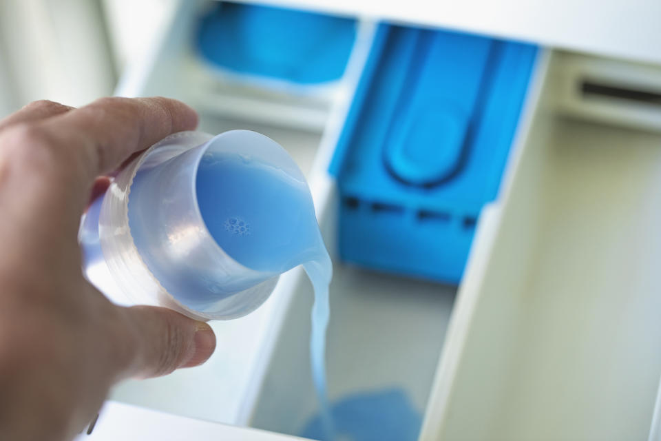 Person pouring liquid detergent into a washing machine dispenser drawer