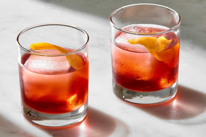 two negronis in rocks glasses, garnished with an orange peel inside of the glass.