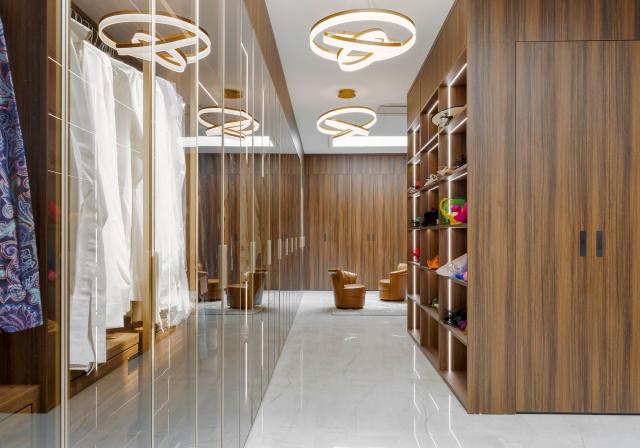 walk in closet with built in cubes for clothes and a hanging closet opposite with clear doors and two small leather chairs in the far background and large circular light fixtures