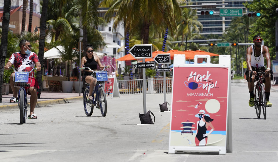 Bike riders ride past a "Mask Up Miami Beach," sign, Tuesday, Aug. 11, 2020, in Miami Beach. Florida added at least 276 fatalities to its coronavirus death toll on Tuesday, a new state record. (AP Photo/Wilfredo Lee)