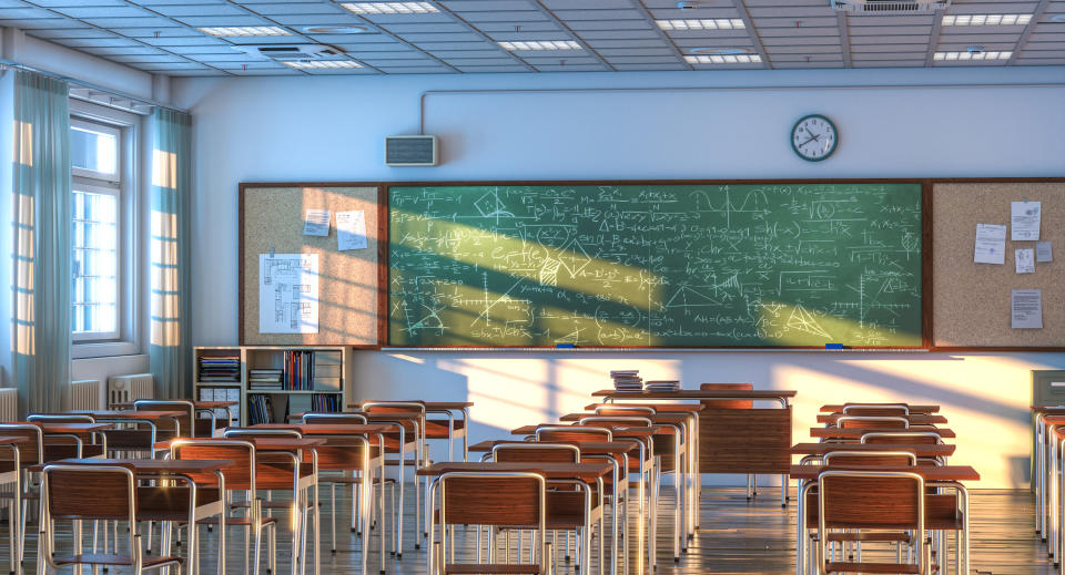 An empty classroom with several rows of desks and chairs facing a chalkboard