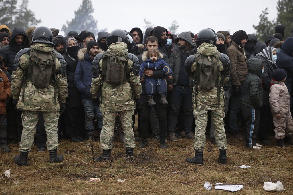 Belarusian service personnel stand in front of migrants at the border (BELTA/AFP/Getty)